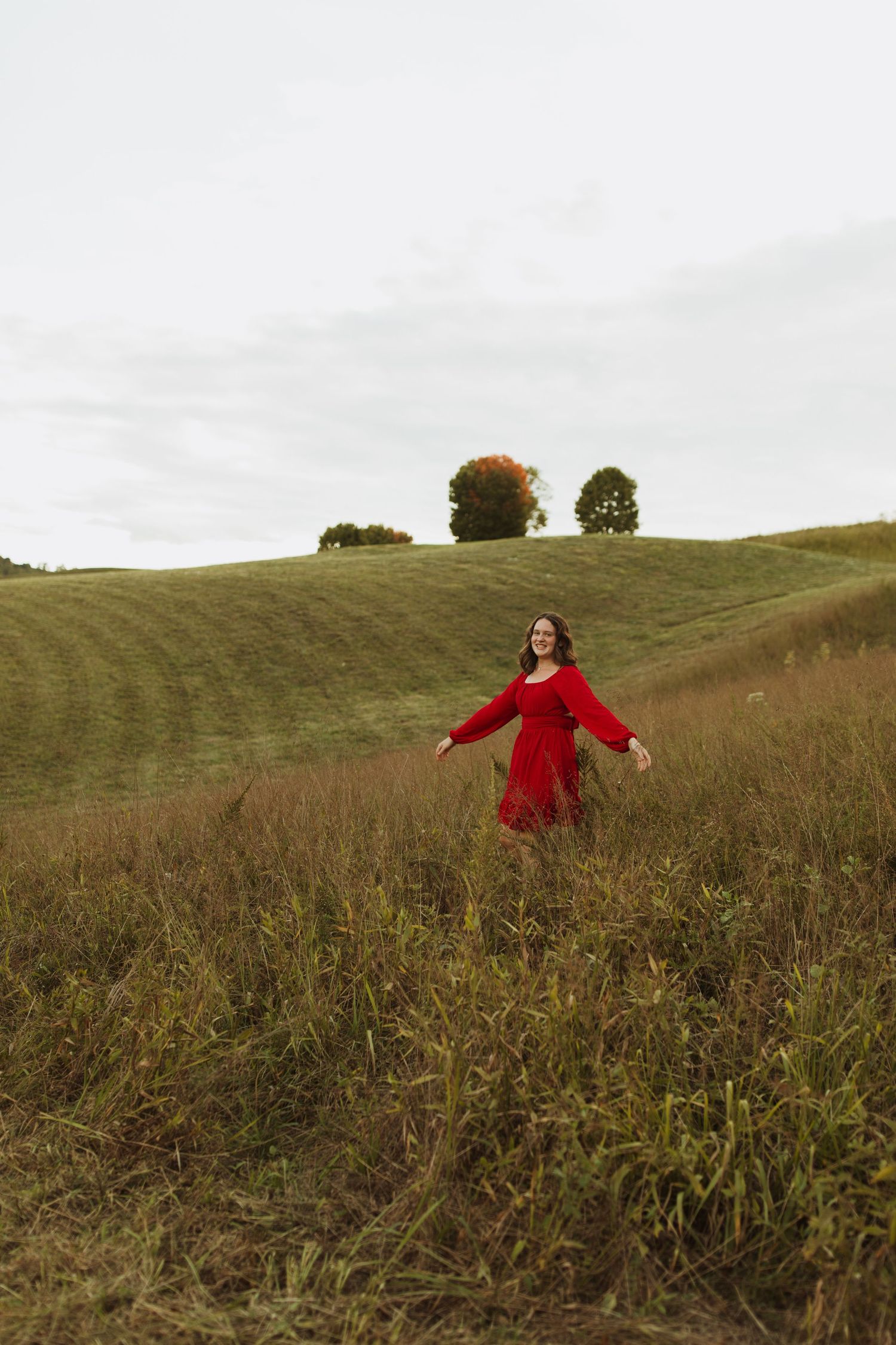 Person in flowing red dress spins freely on a rolling green hillside at dusk.
