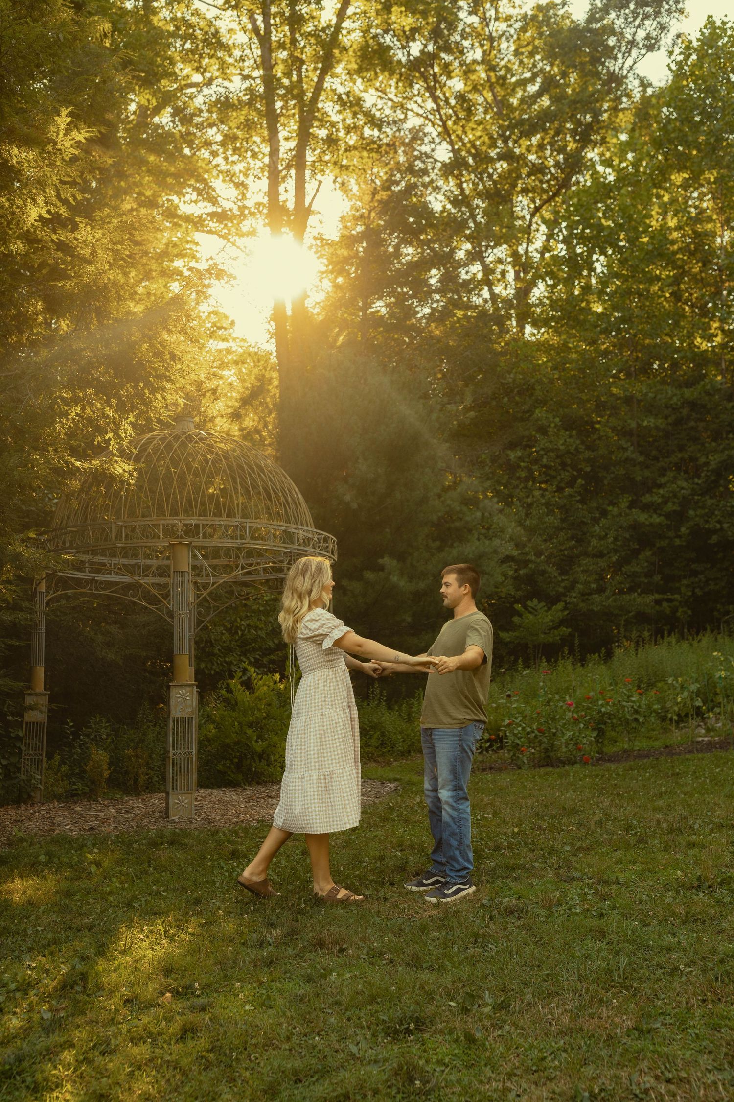 Dancing couple in a garden with a metal gazebo during sunset.
