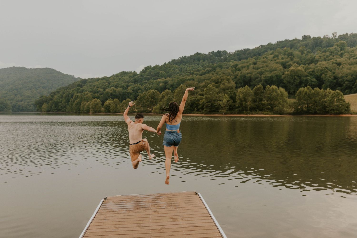 Two people jumping off a wooden dock into a serene mountain lake.