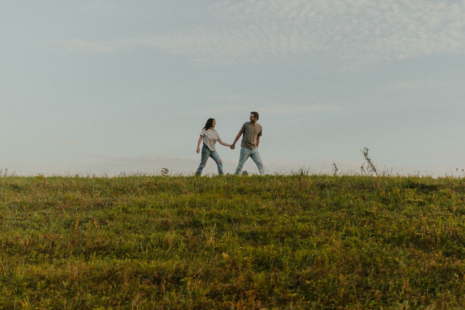 Silhouettes of two people walking together on a grassy hilltop against a cloudy sky during golden hour.