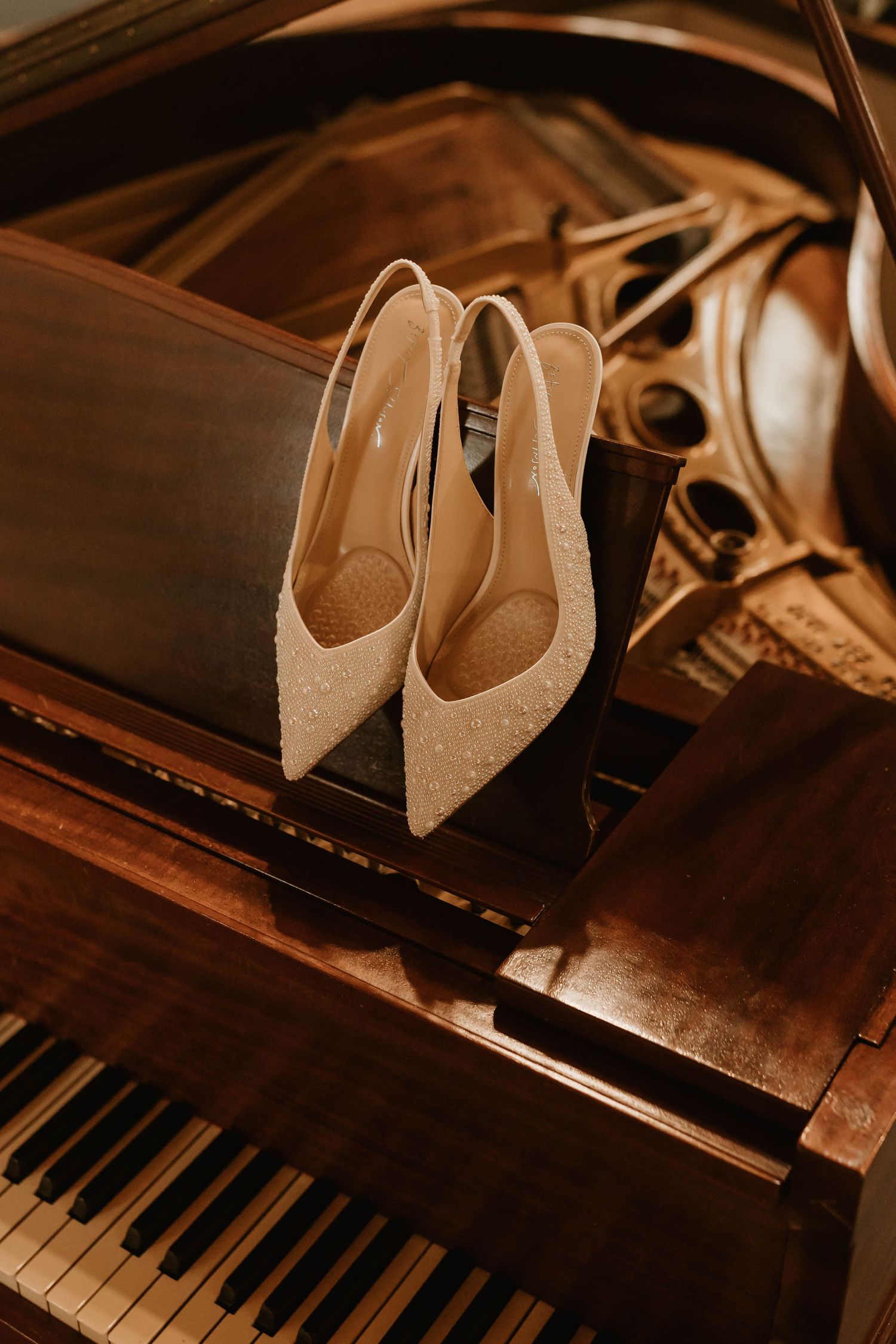 White bridal shoes displayed on a grand piano in warm lighting.