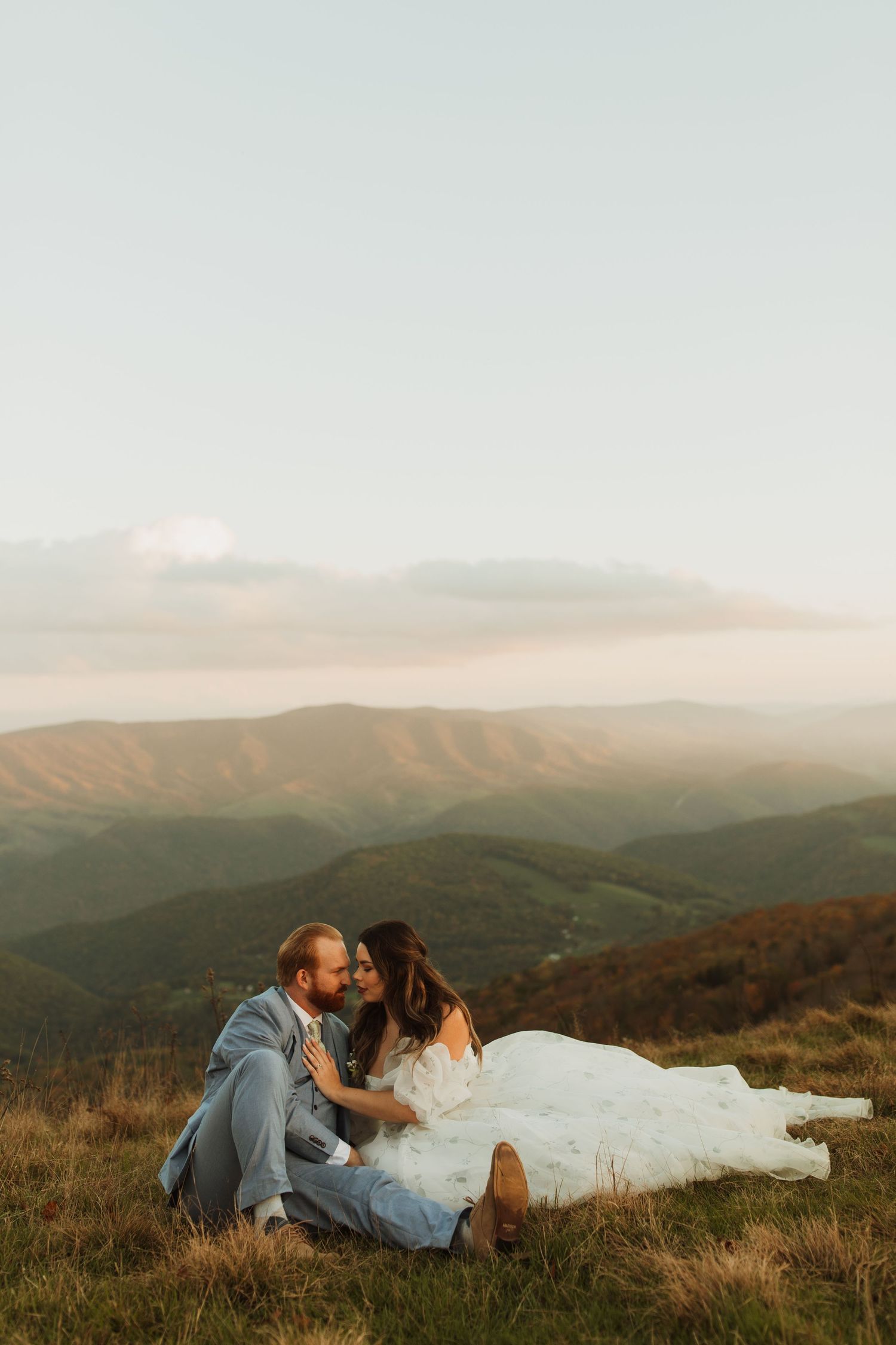 Newlyweds share an intimate moment on a mountaintop during golden hour.