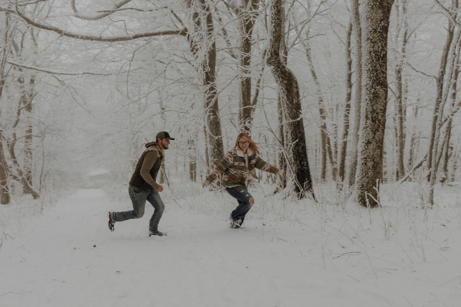 Two people playfully running through a snowy winter forest.