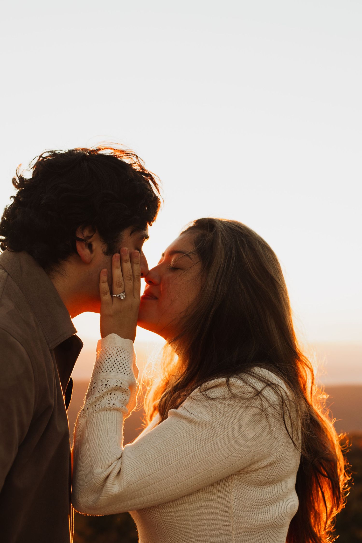 A romantic sunset moment between two people in white sweaters against a bright background.