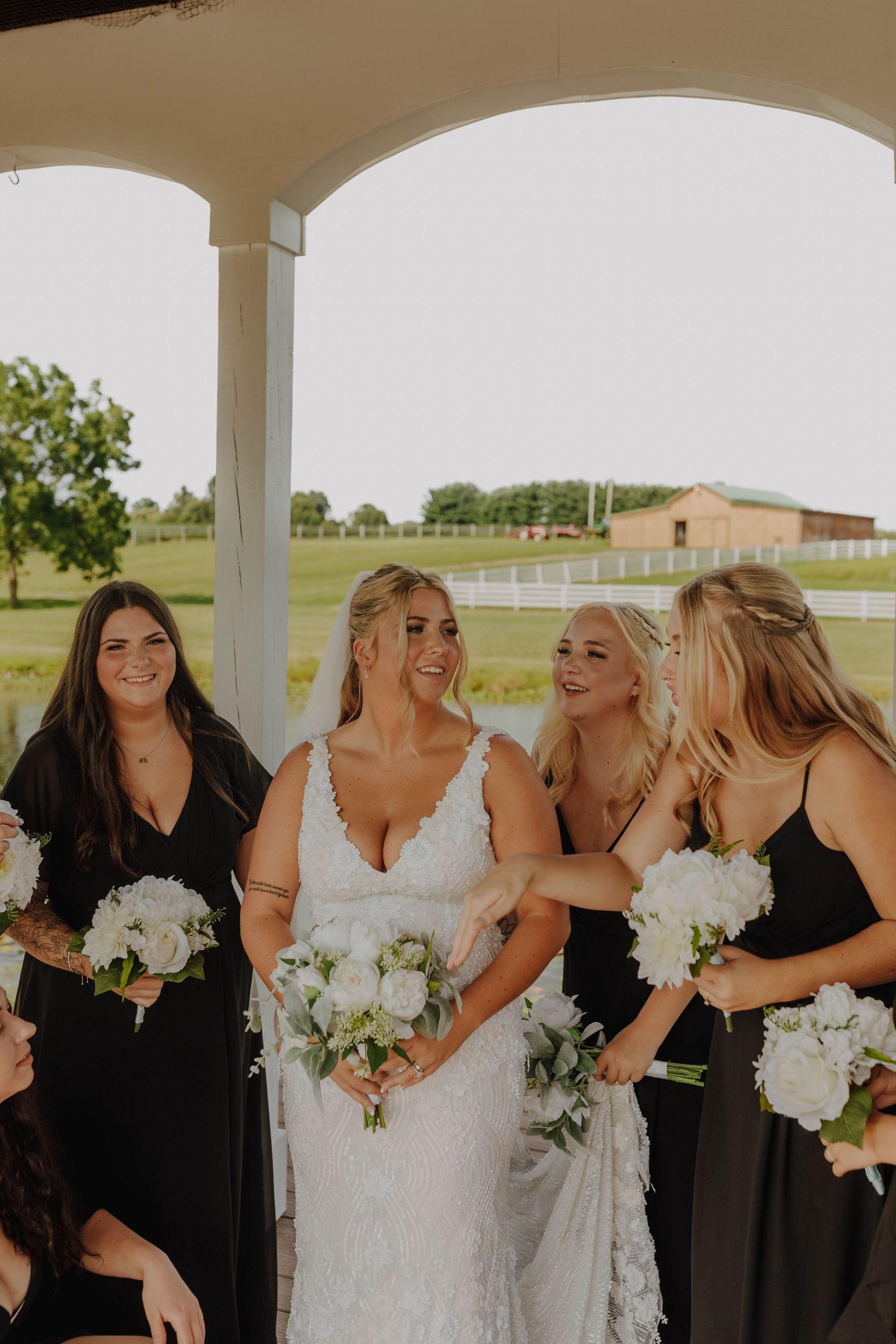 Bridal party in black dresses holding white bouquets while sharing a joyful moment under a porch.