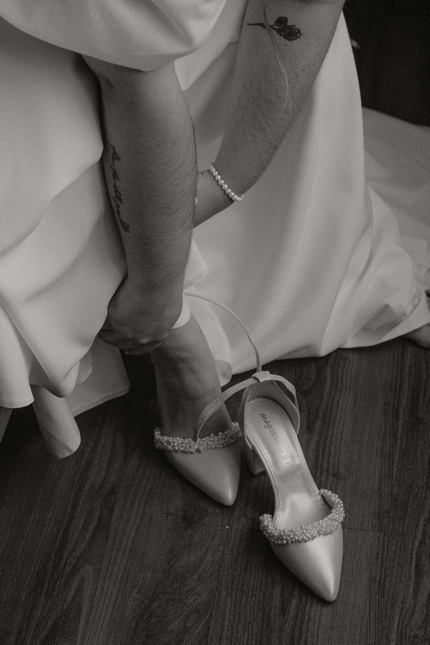 Close-up of sparkly bridal shoes and white dress hem on wooden floor.