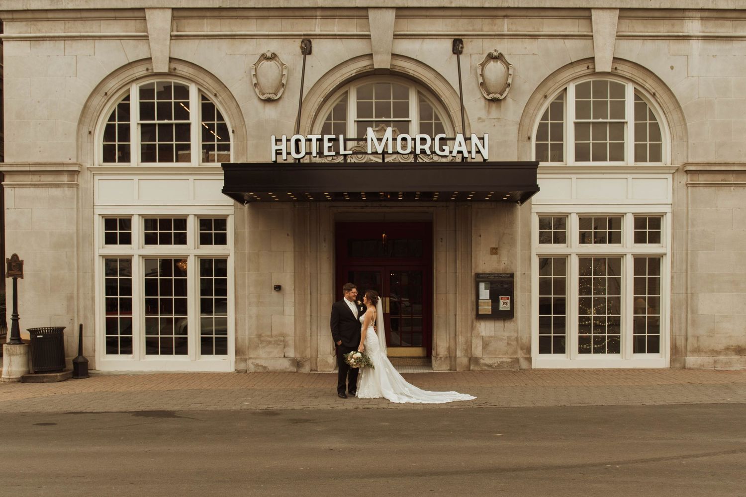 A couple embraces under the classic Hotel Morgan entrance marquee in warm tones.