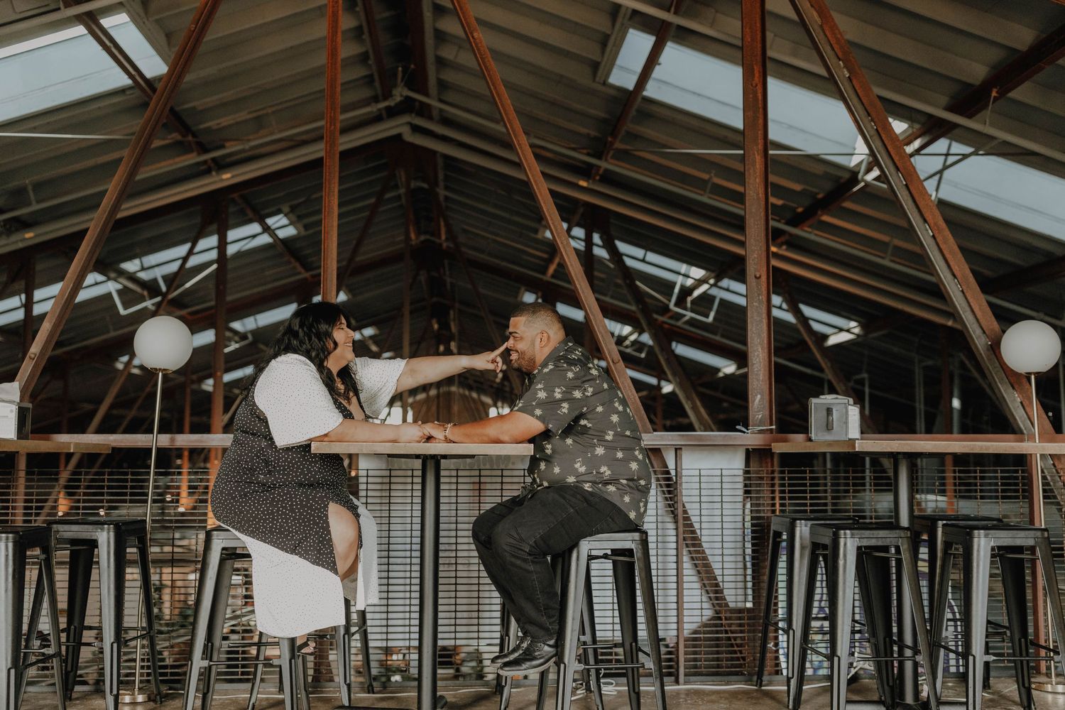 Couple enjoying drinks together at high-top tables in rustic venue with exposed beams.
