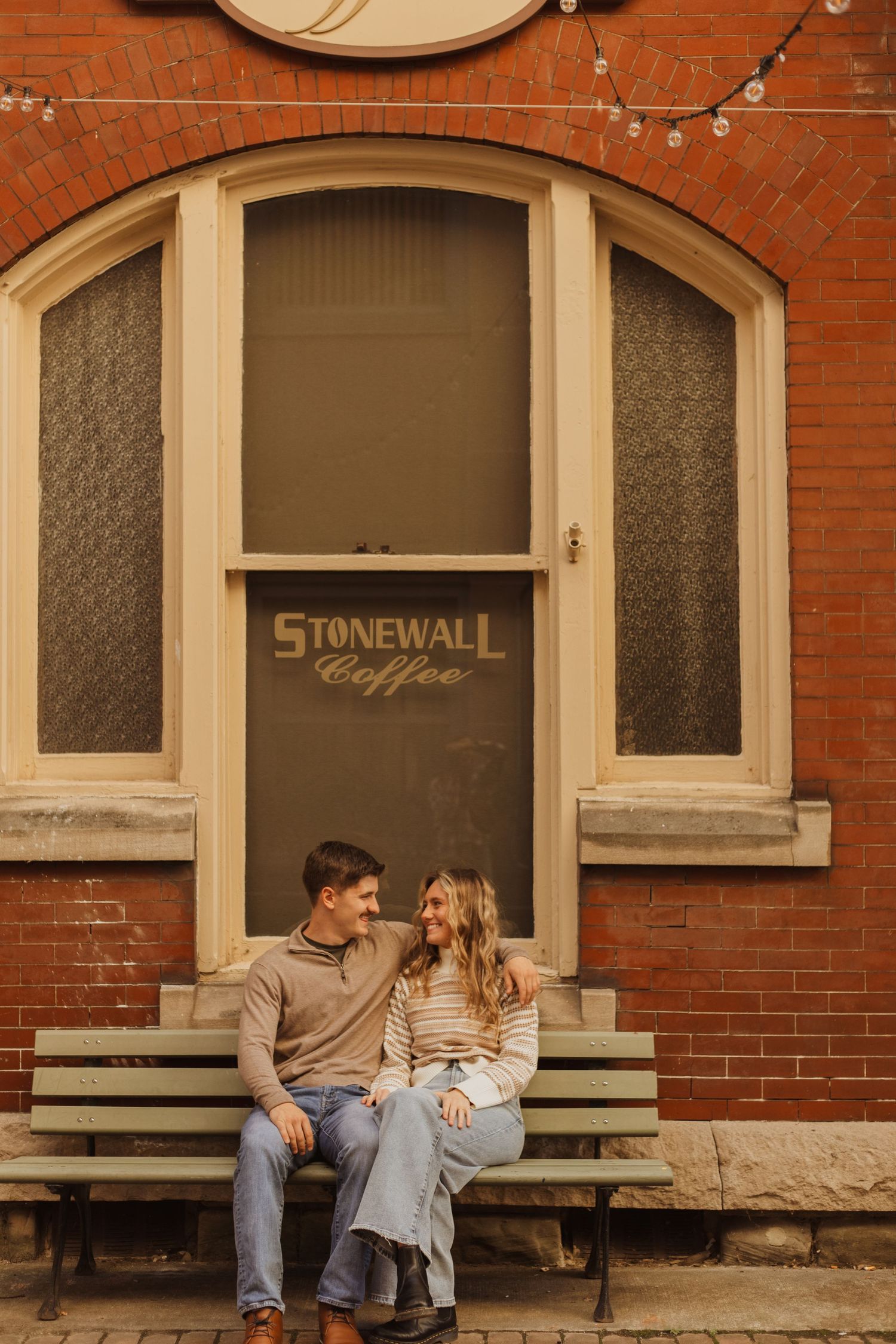 Couple sitting on bench outside Stonewall Coffee entrance with red brick facade.