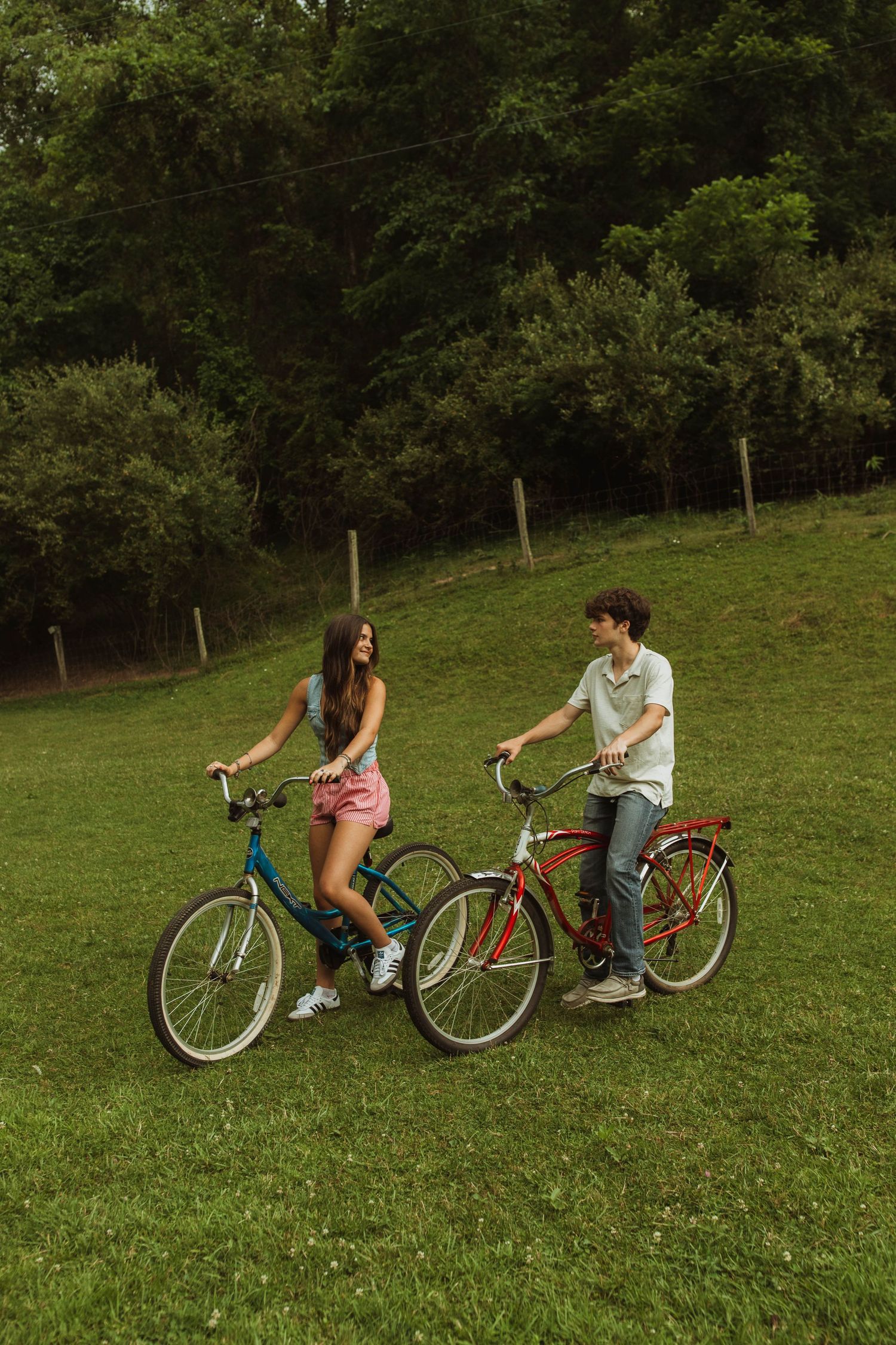 Two people riding vintage bicycles on a grassy hillside.