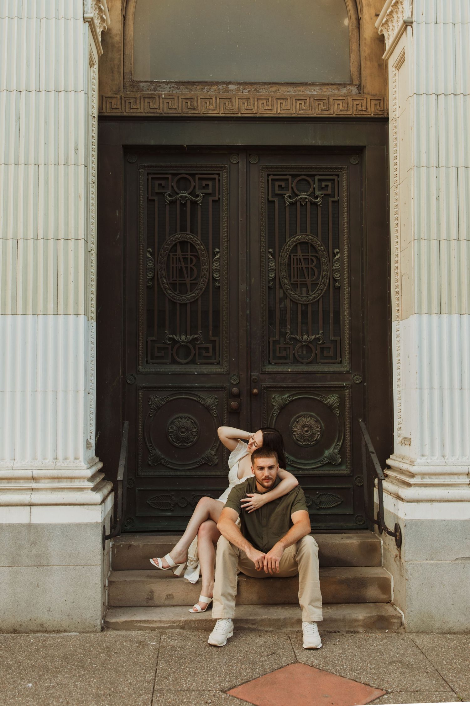 A couple posing on steps in front of an ornate vintage door with decorative ironwork.