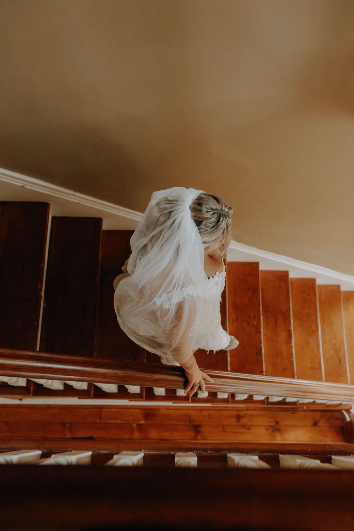 Looking down wooden staircase at flowing white wedding dress and veil.