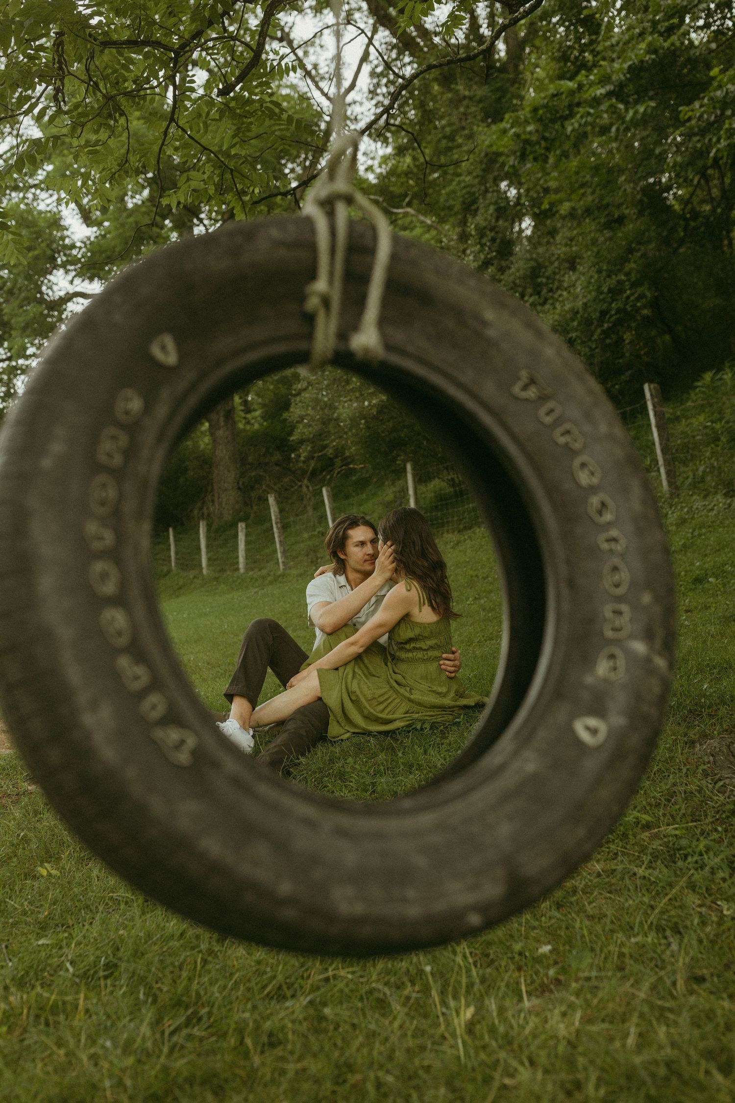 Creative photo composition through a tire swing frame showing a couple relaxing on grass.