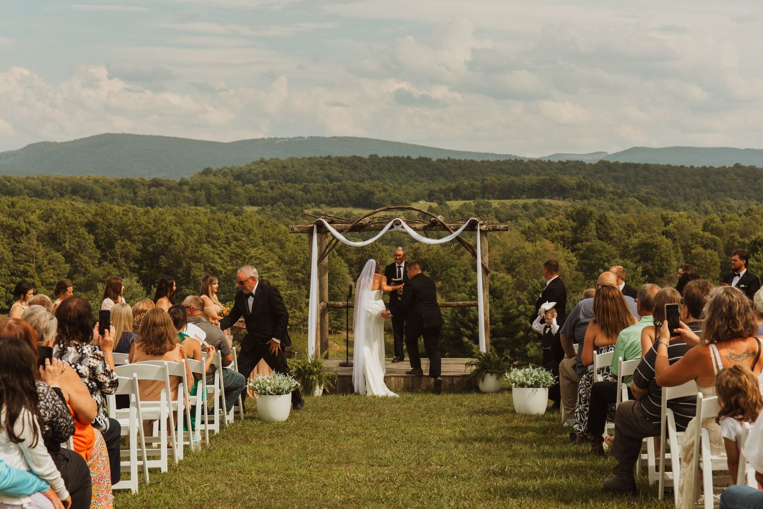 Outdoor wedding ceremony setup with mountain views and white chairs on a hilltop.