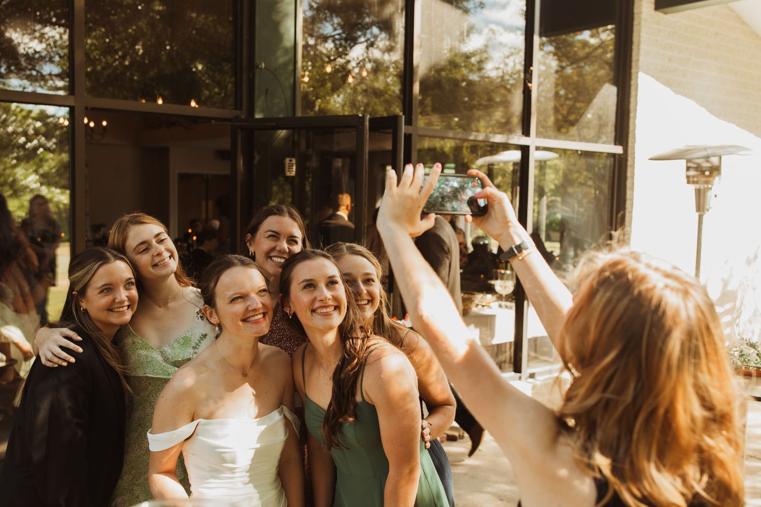 Wedding party celebrates with joyful expressions in front of a glass building.