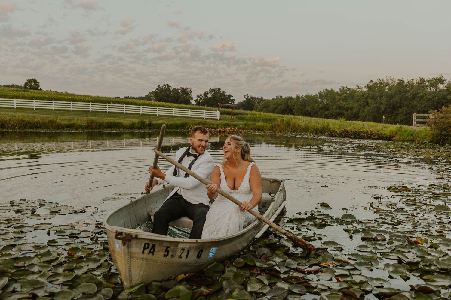 A couple rowing through a peaceful pond filled with lily pads at golden hour.