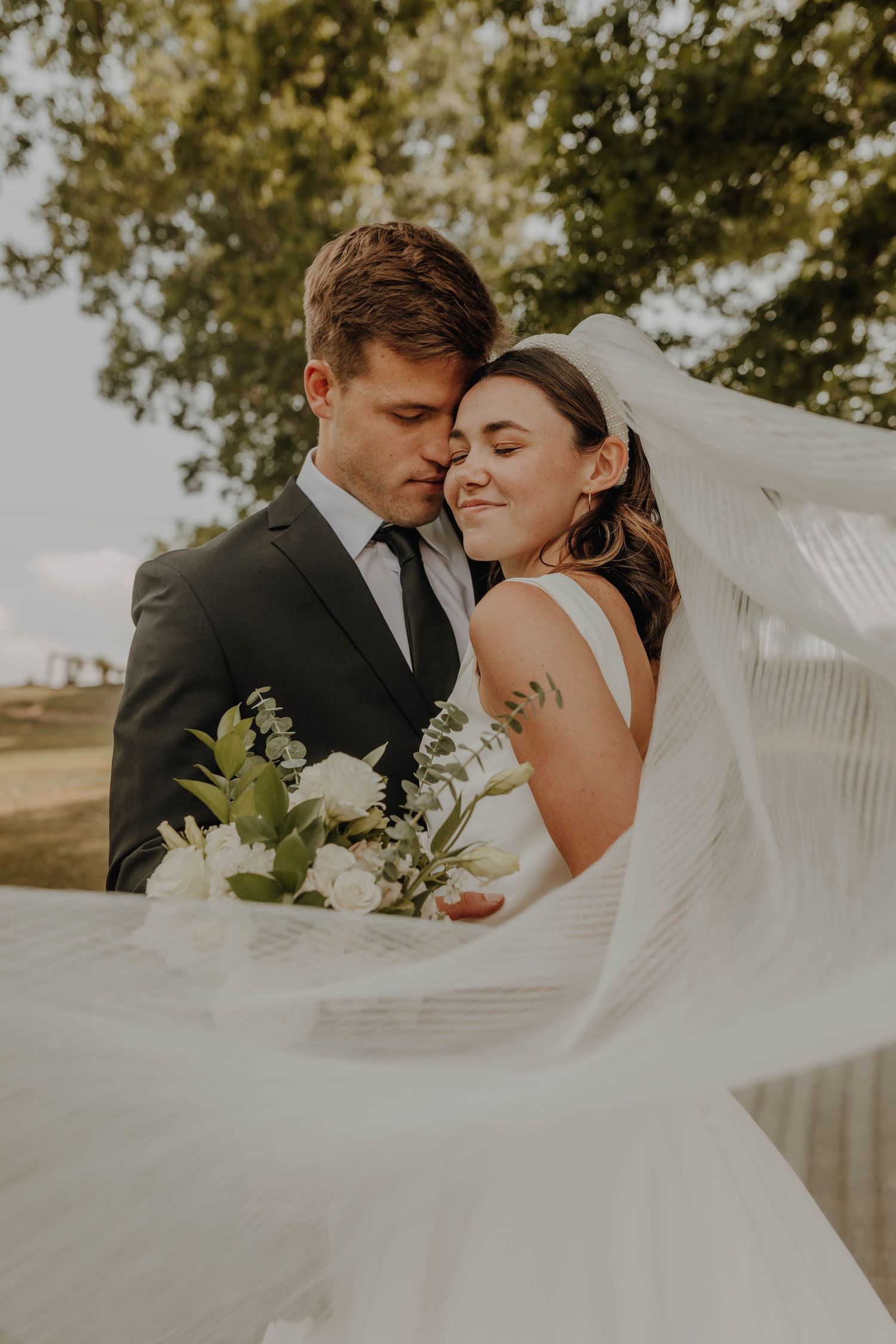 An intimate wedding portrait with flowing veil and natural golden lighting.