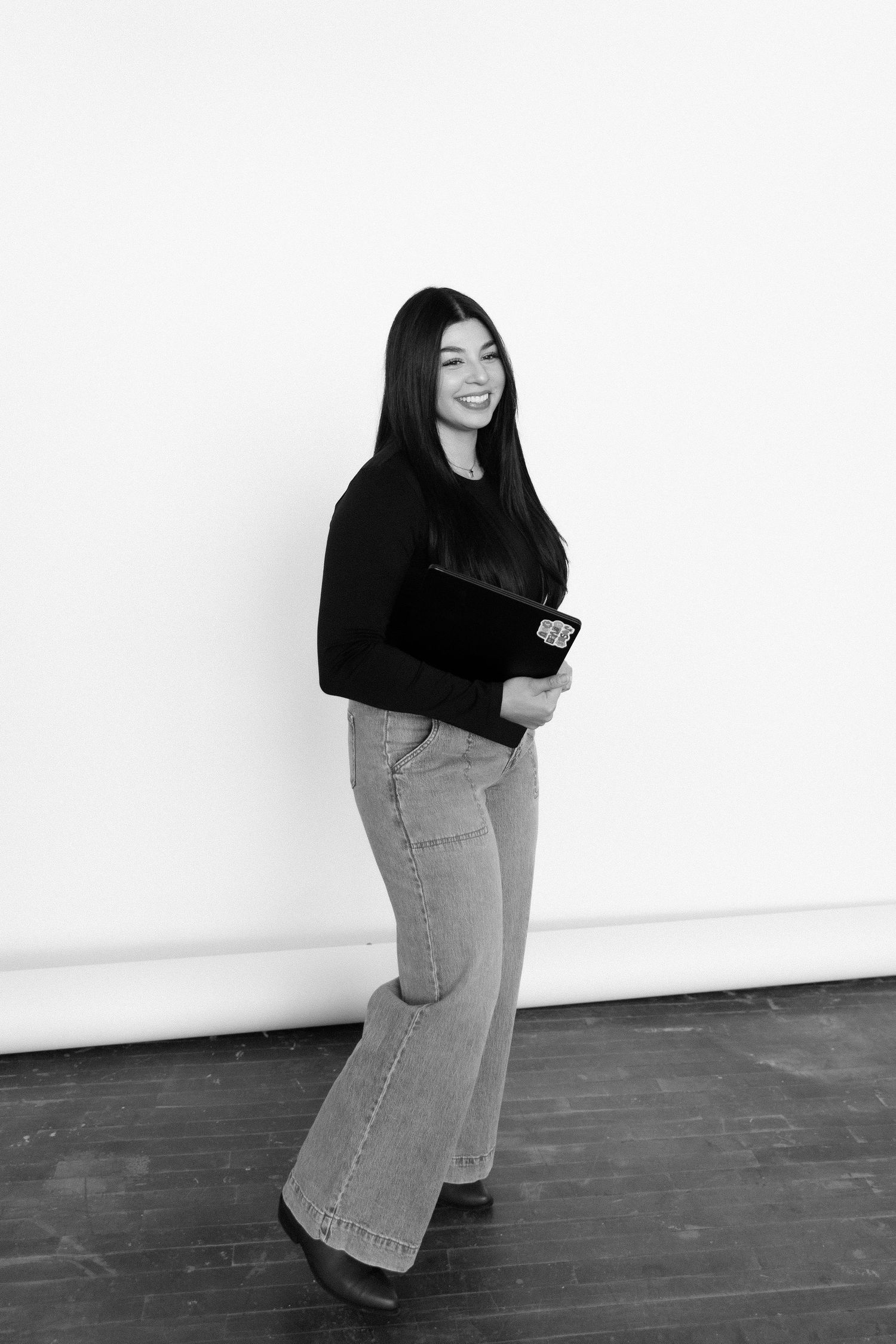 Photographer in casual attire poses with camera equipment against white studio wall.