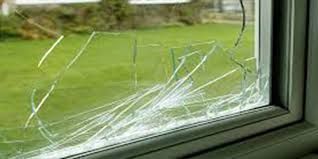 A cracked window pane with spiderweb fractures overlooking a green lawn in the background.