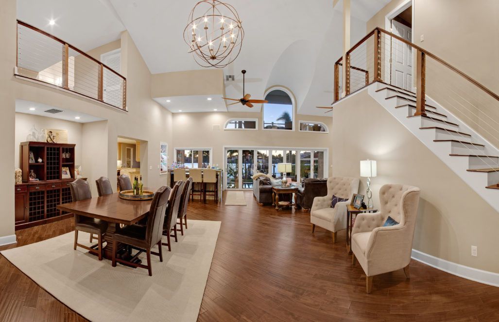 Modern open concept living room and dining area with high ceilings, hardwood floors, and elegant chandelier lighting.