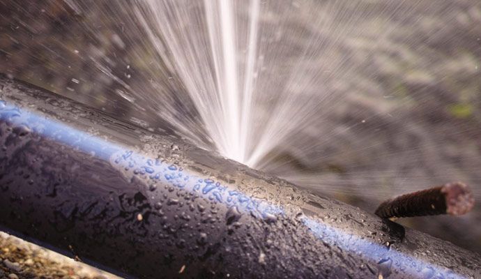 Water spraying from a leaking black pipe showing pressure loss through a crack.