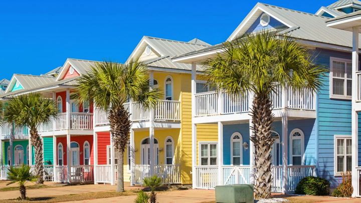 Colorful coastal beach houses with palm trees and porches in vacation community style architecture.