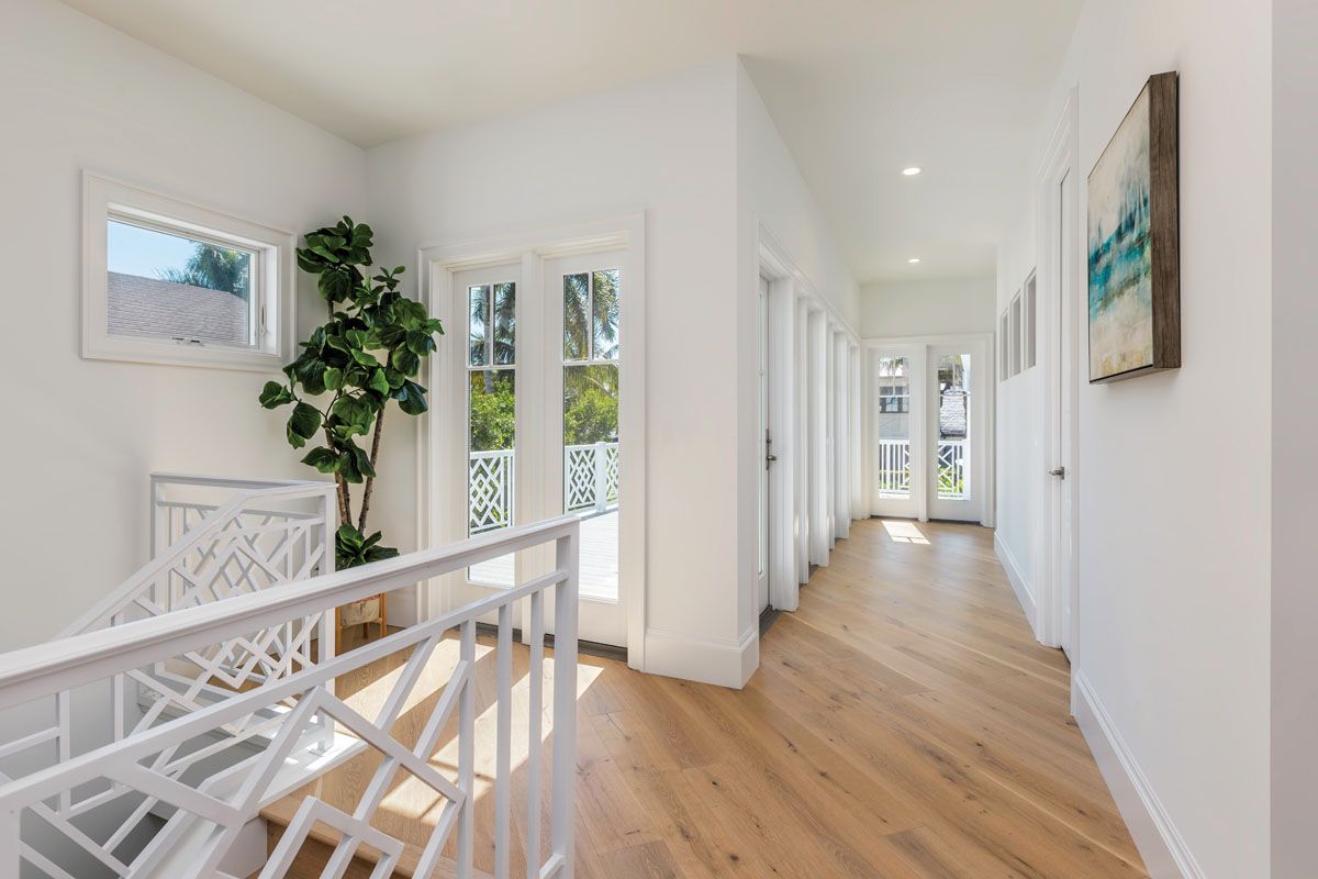 Bright modern hallway with white walls, hardwood flooring, and large windows featuring geometric railings and potted plants.