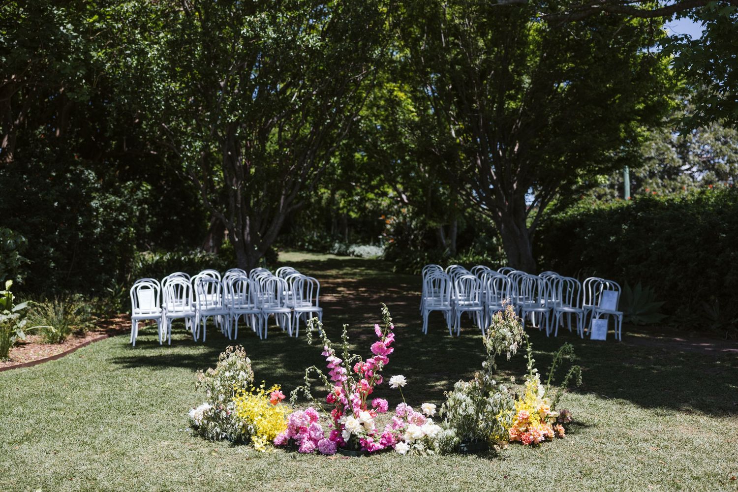 Garden wedding ceremony setup with white chairs and vibrant floral decorations.