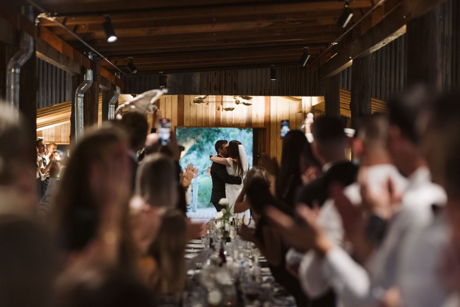 Wedding ceremony in a rustic barn venue with guests watching and string lights overhead.