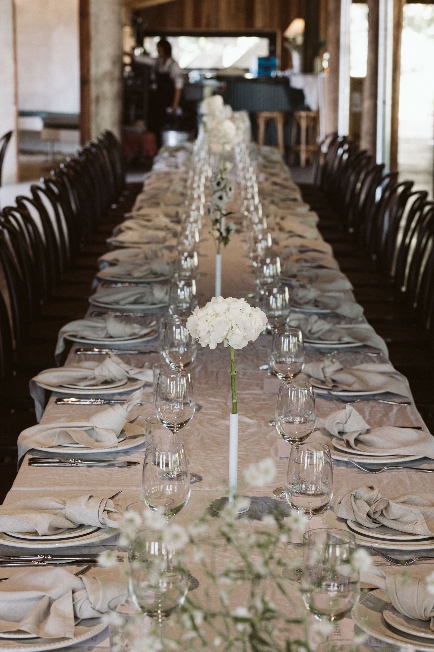 Long dining table set for elegant wedding reception with white floral arrangements and glassware.