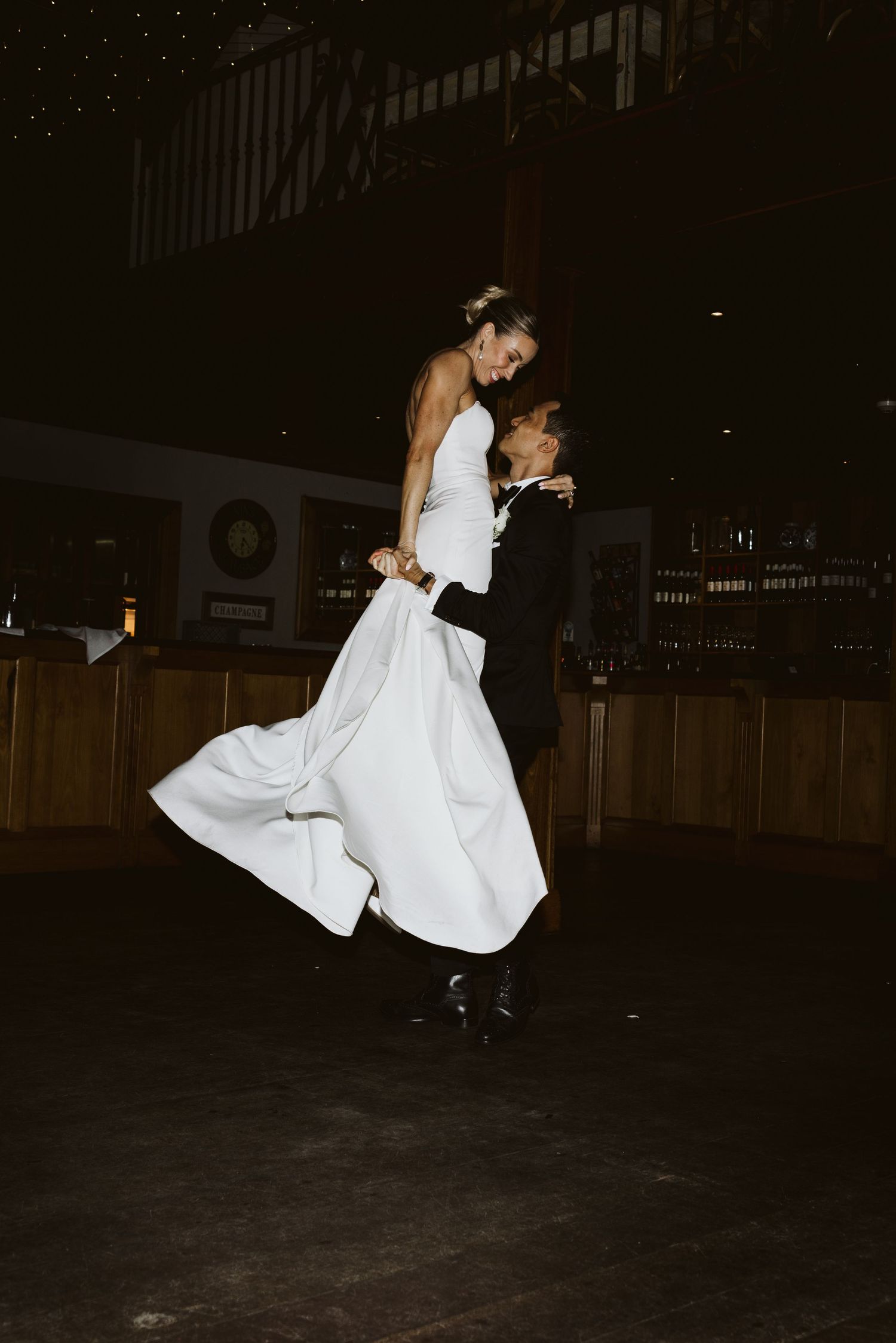 A couple performs a dramatic dance lift during their wedding reception in a dimly lit venue.