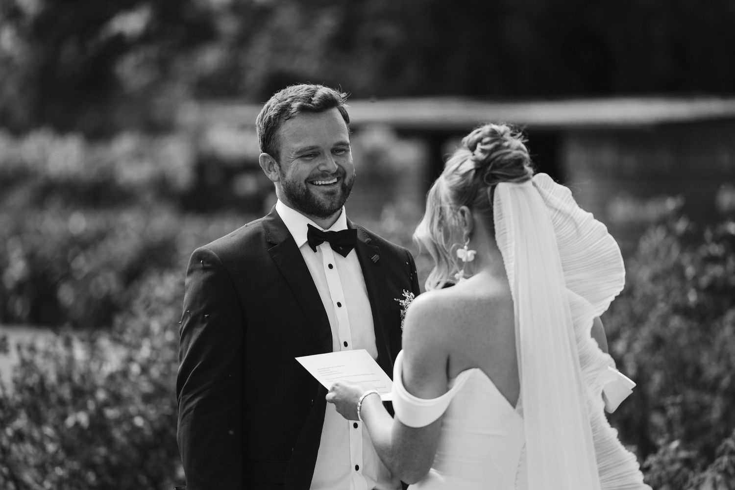 Black and white portrait of wedding couple exchanging vows in garden setting.