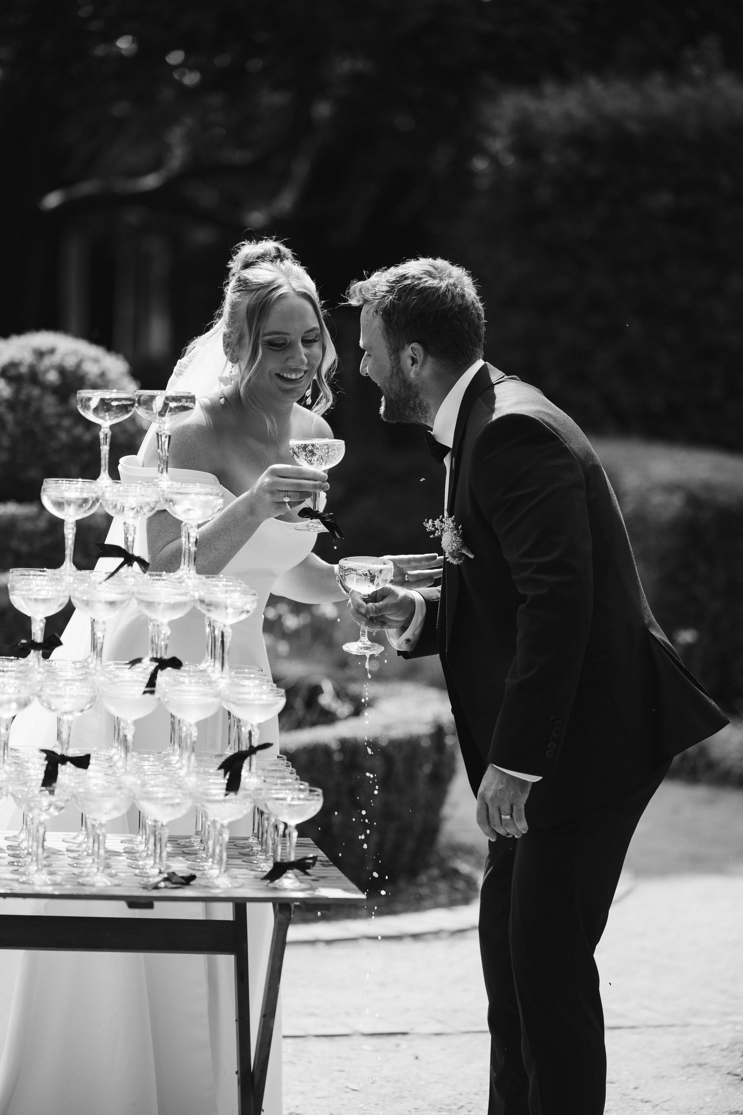 Black and white photo of couple sharing moment at champagne tower during reception.
