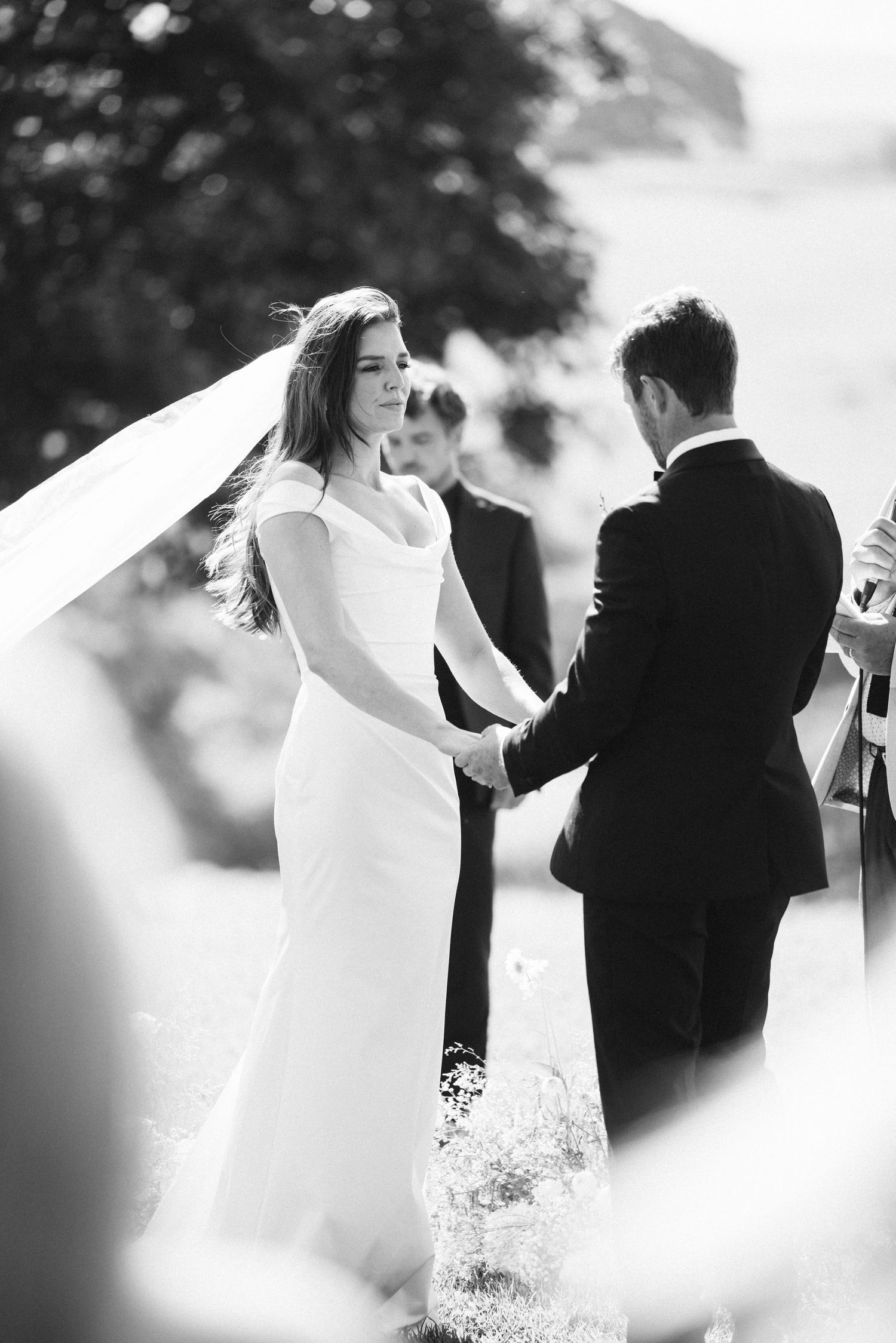 Wedding ceremony under trees with flowing white veil catching the breeze.