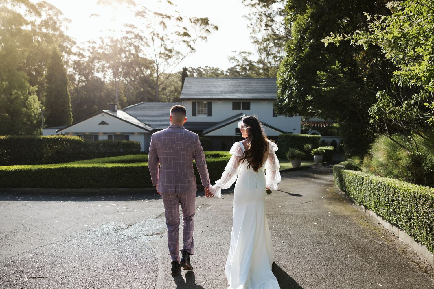 Couple walking hand in hand down a tree-lined suburban street at sunset.