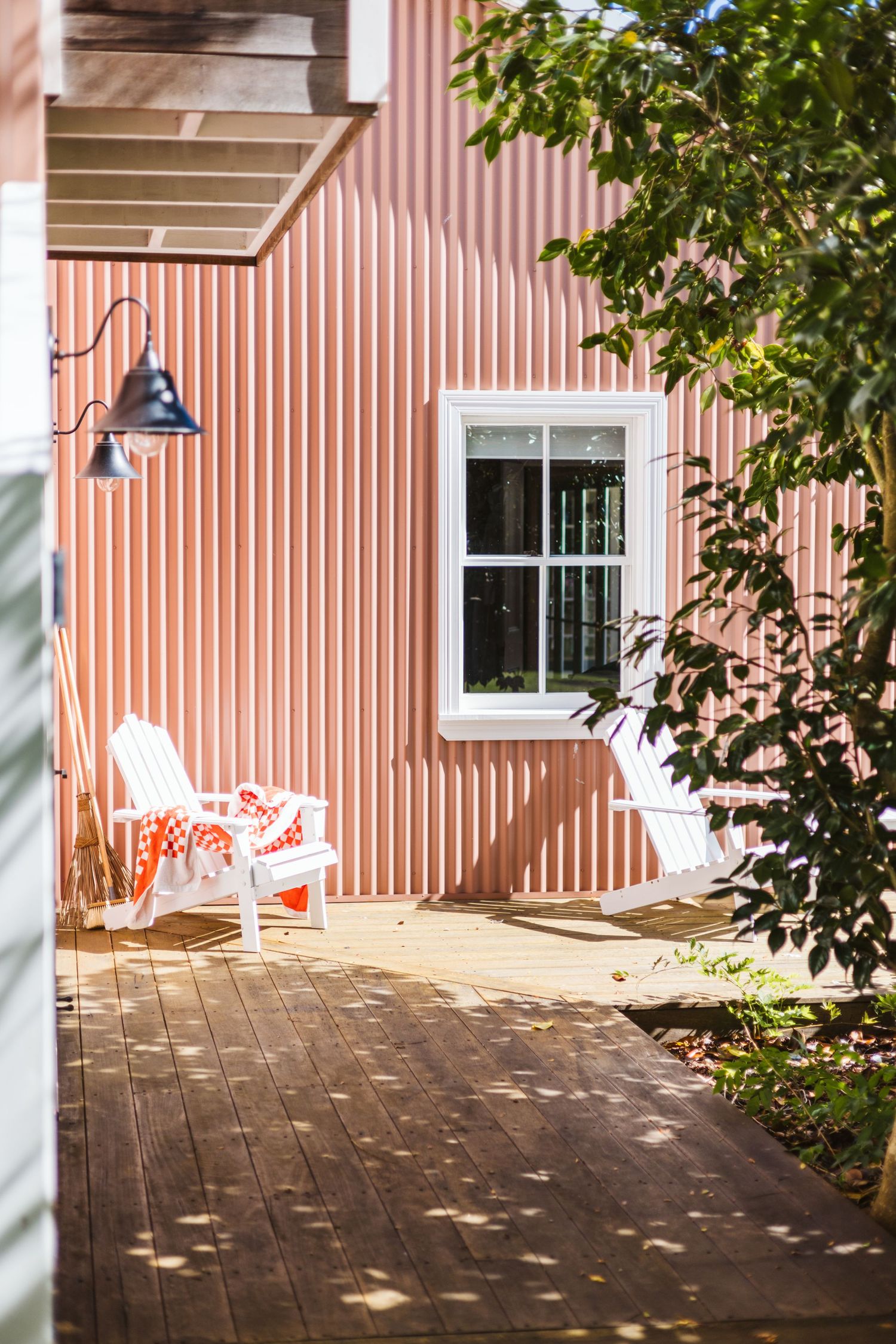 White rocking chair on wooden deck beside coral-colored building with white trim.