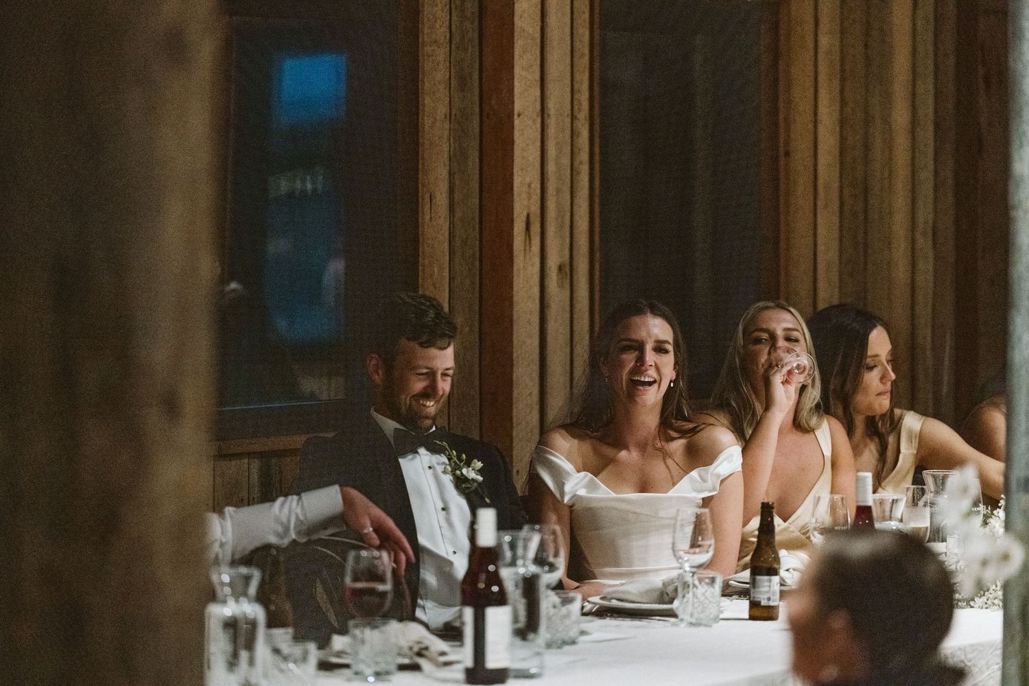 Candid moment during wedding reception speeches in rustic wooden venue.