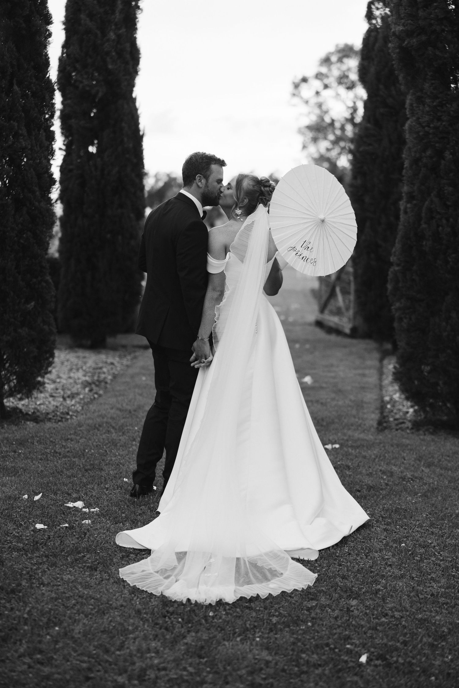 Black and white portrait of couple with parasol among cypress trees.