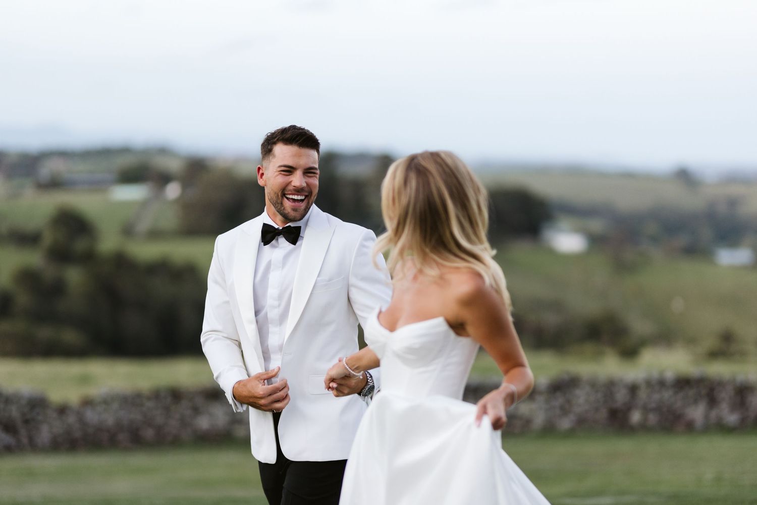 A joyful wedding couple sharing a laugh together on a scenic hilltop.