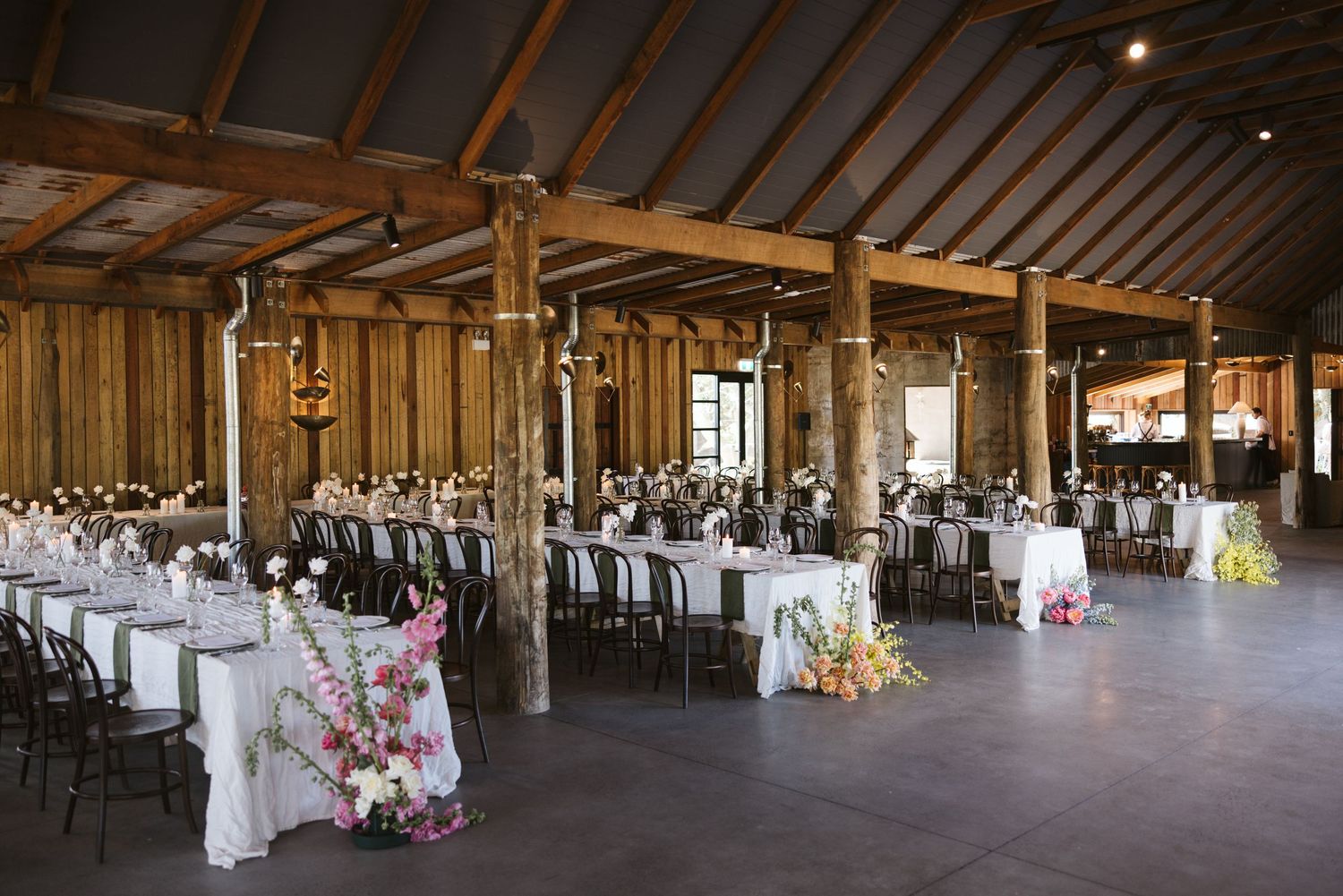 A rustic barn wedding reception venue with long tables set up under wooden beams and pillars.