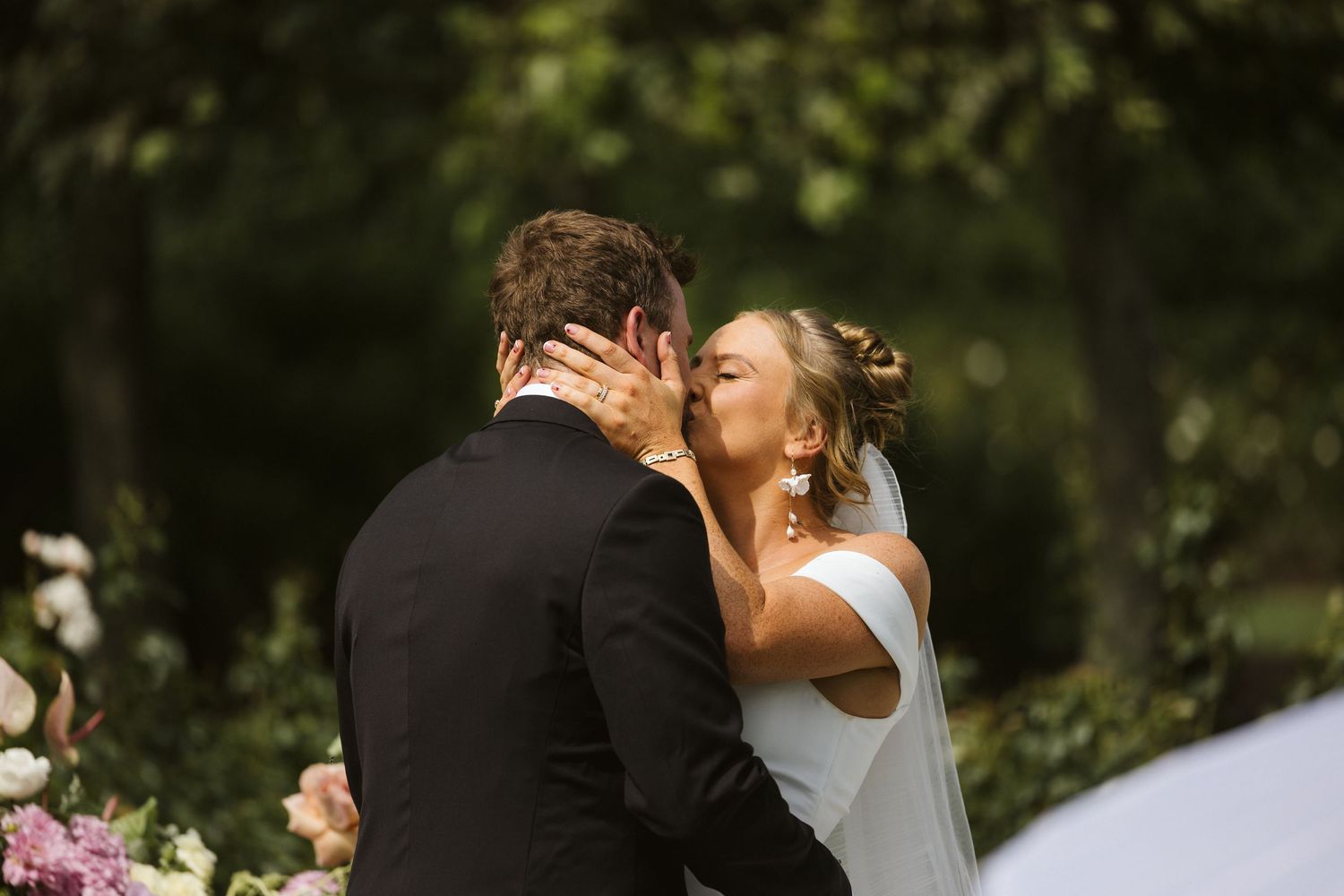 Romantic wedding kiss captured in natural garden setting.