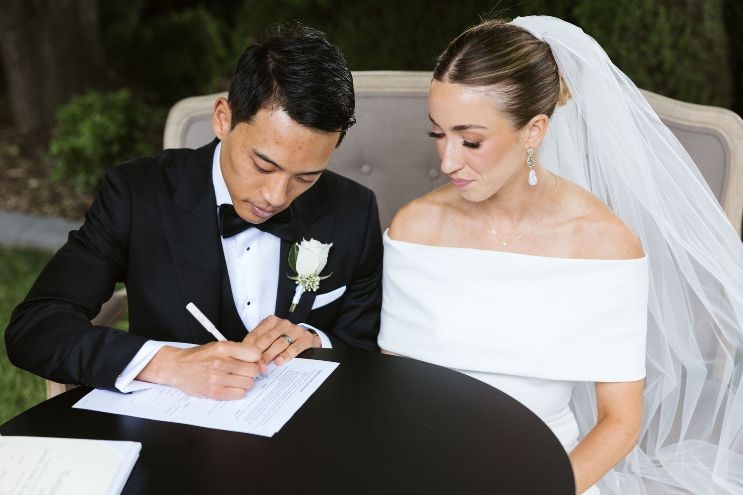 Couple signing wedding documents at outdoor ceremony with elegant attire.