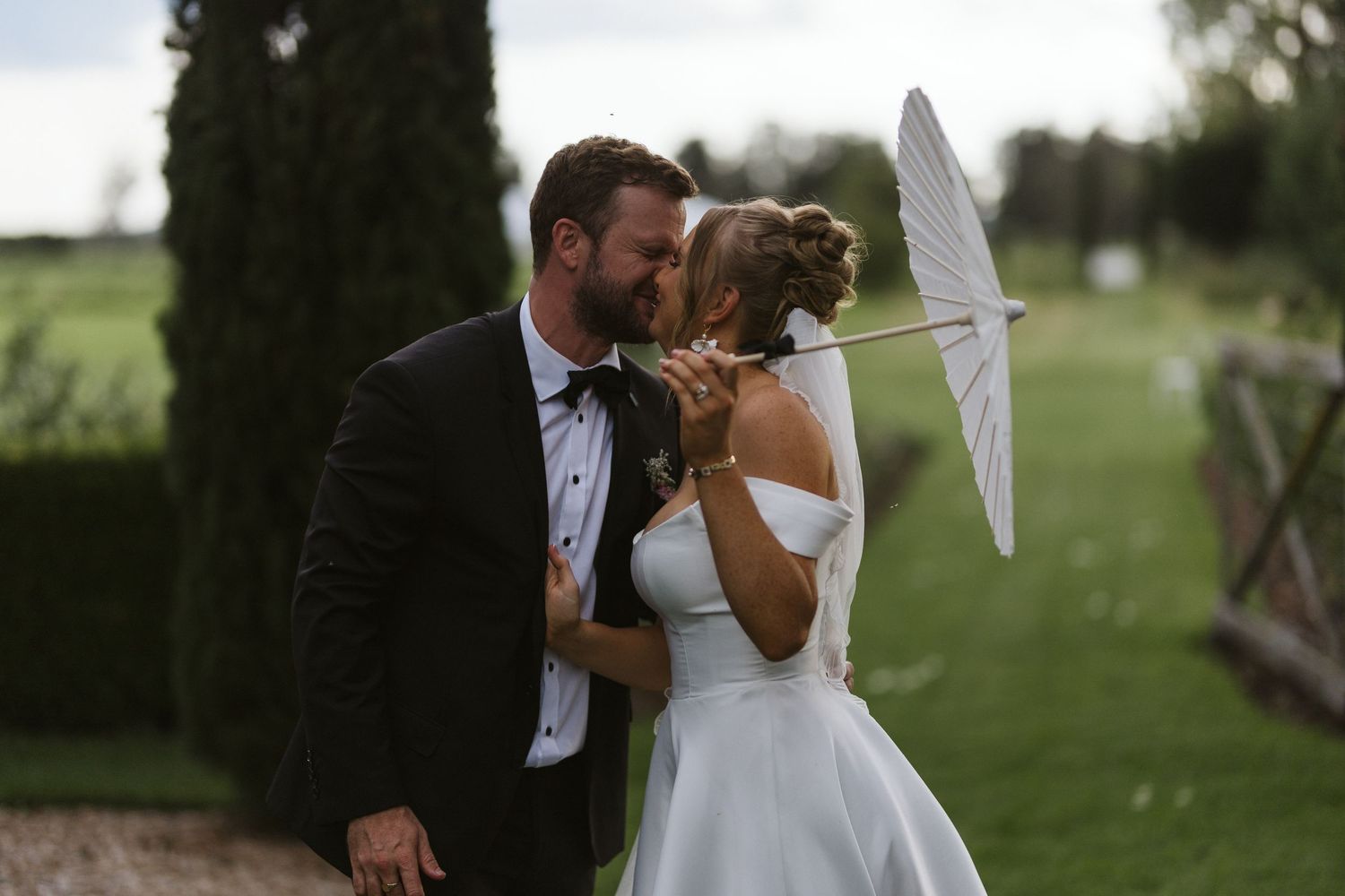 Romantic couple shares intimate moment under white parasol in garden setting.