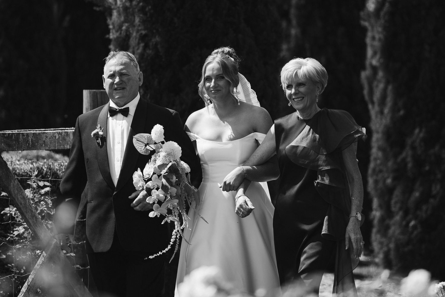 A black and white photograph capturing a wedding moment in a formal garden setting.