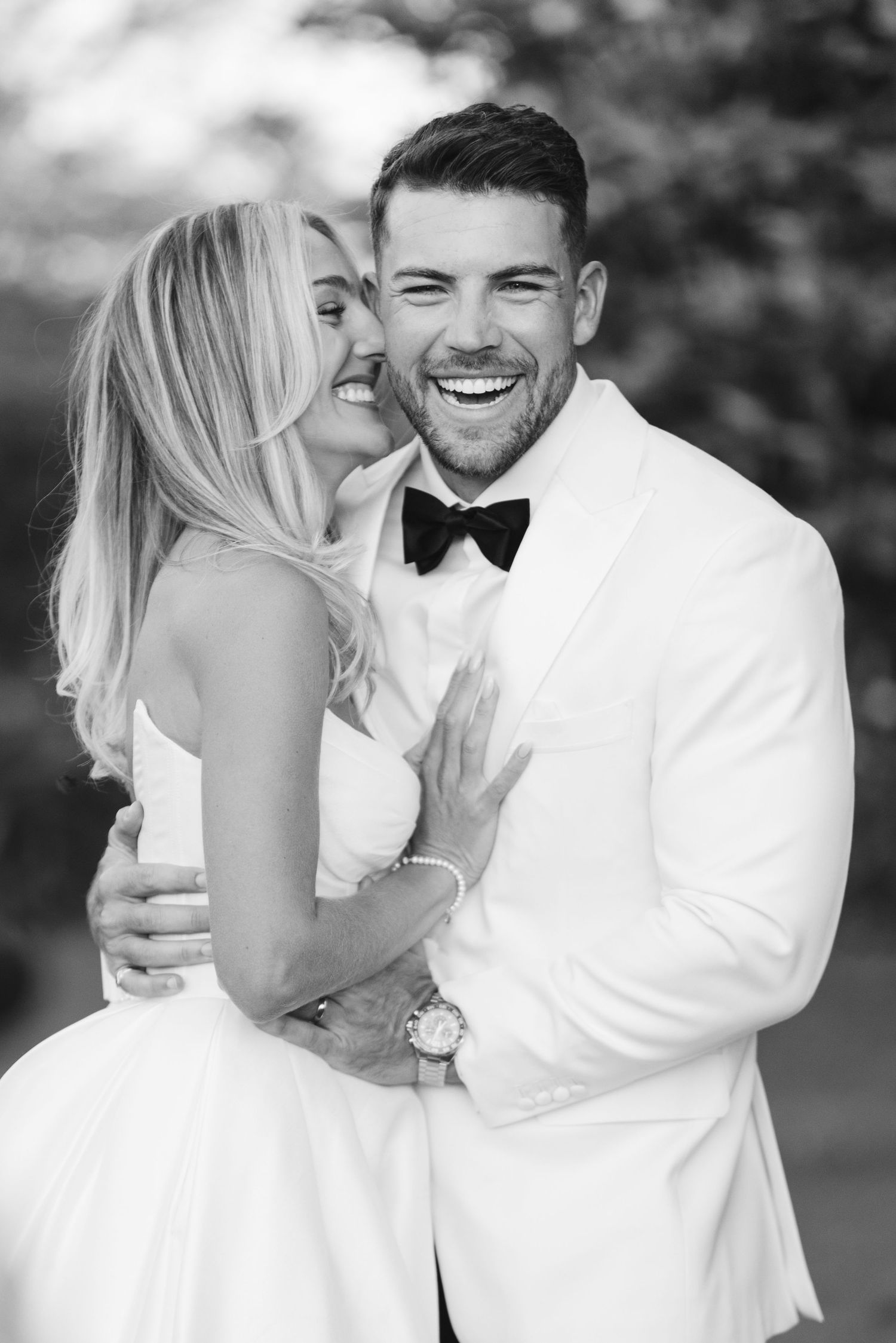A joyful bride and groom share a candid laughing moment in black and white formal wedding attire.