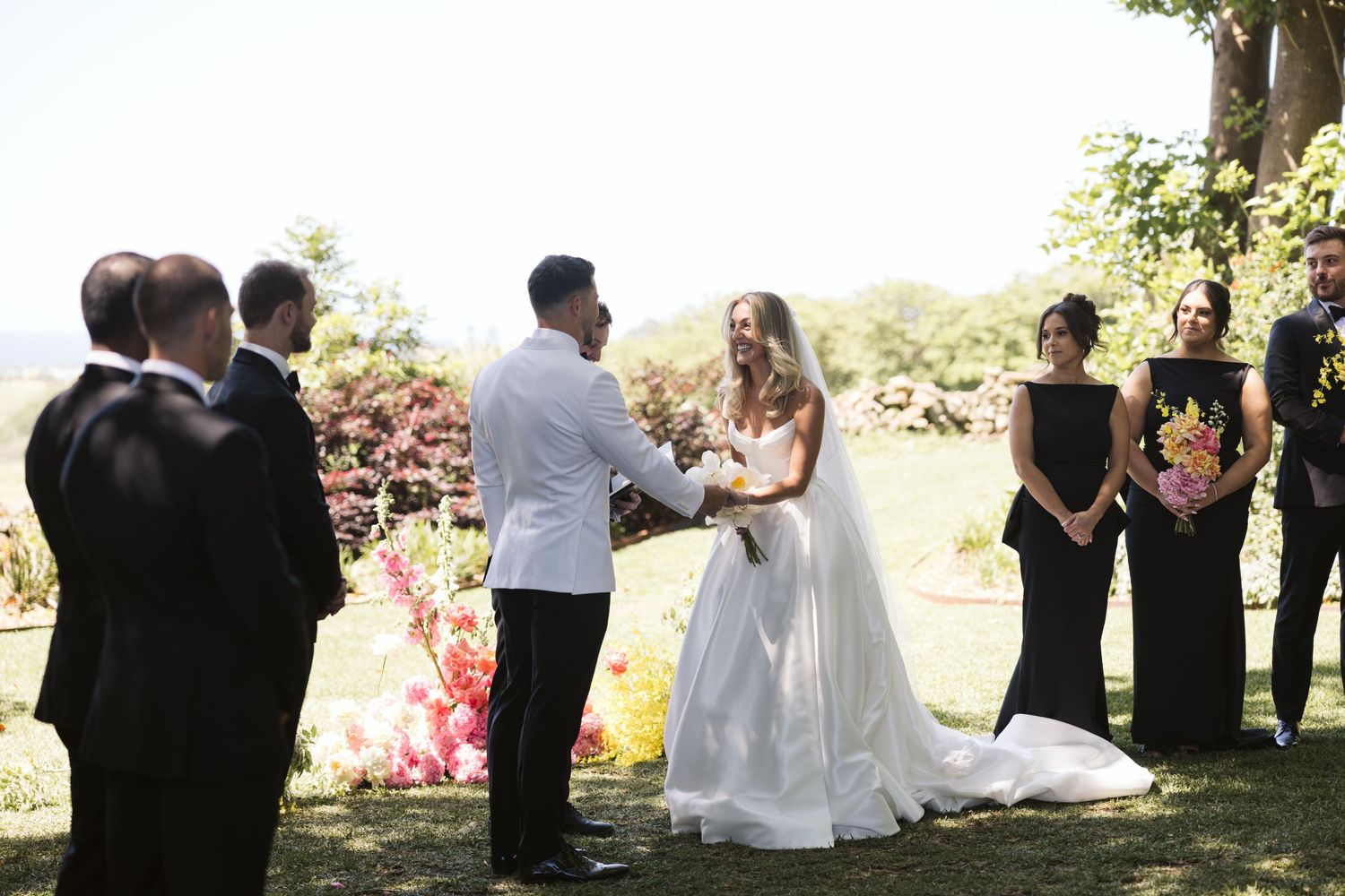 Outdoor garden wedding ceremony with guests watching couple exchange vows.