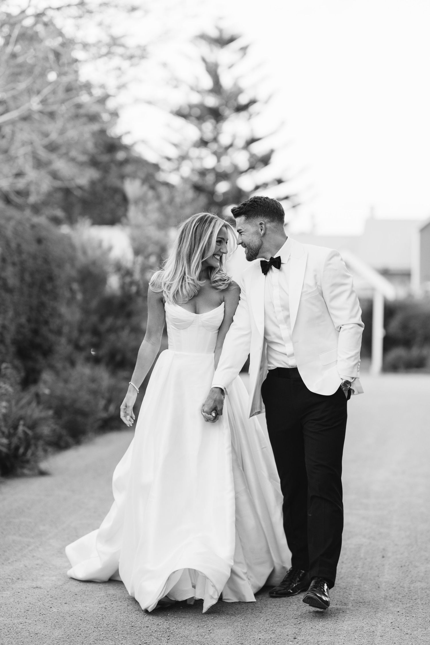 Black and white portrait of couple in elegant wedding attire walking together.