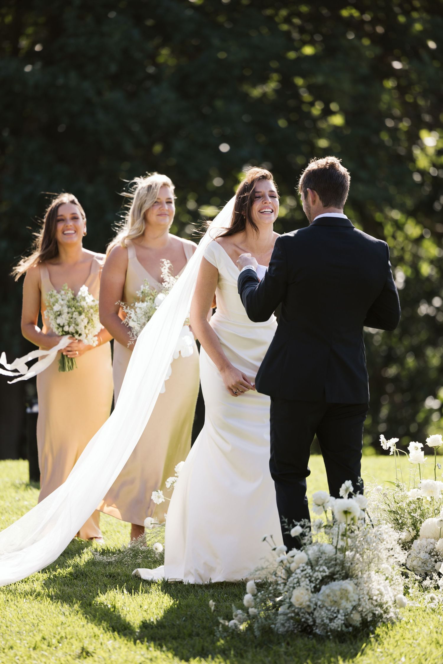 Outdoor wedding ceremony with bridesmaids in champagne dresses and floral arrangements decorating the lawn.