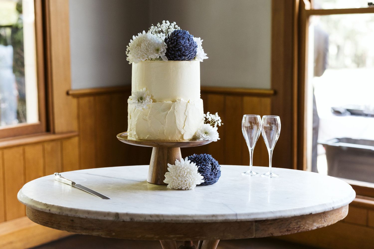 A two-tier white wedding cake decorated with navy and white flowers.