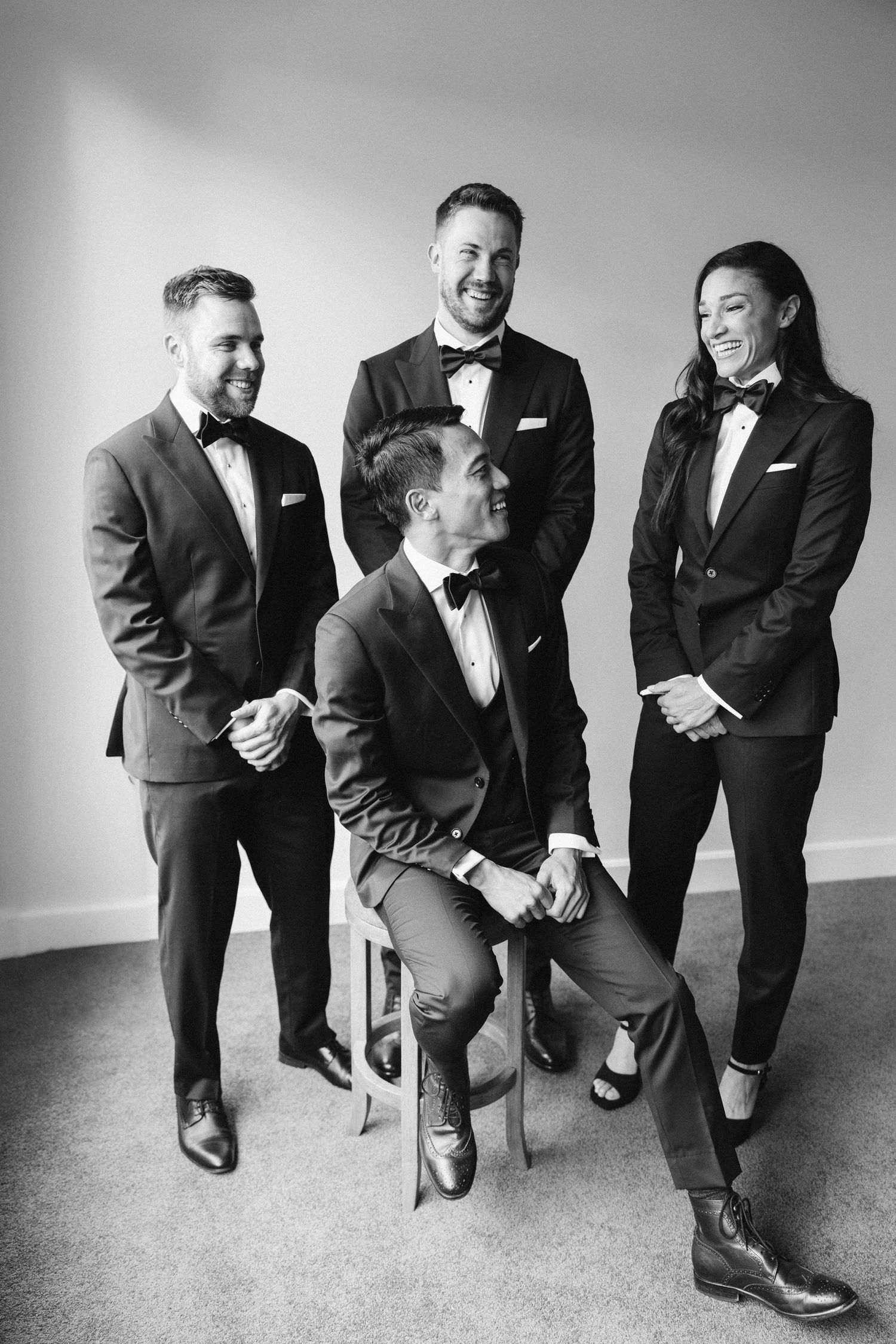Four wedding party members in black tuxedos pose together for a formal portrait.